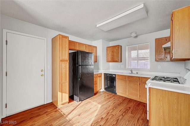 kitchen featuring light wood-type flooring, black appliances, under cabinet range hood, a sink, and light countertops