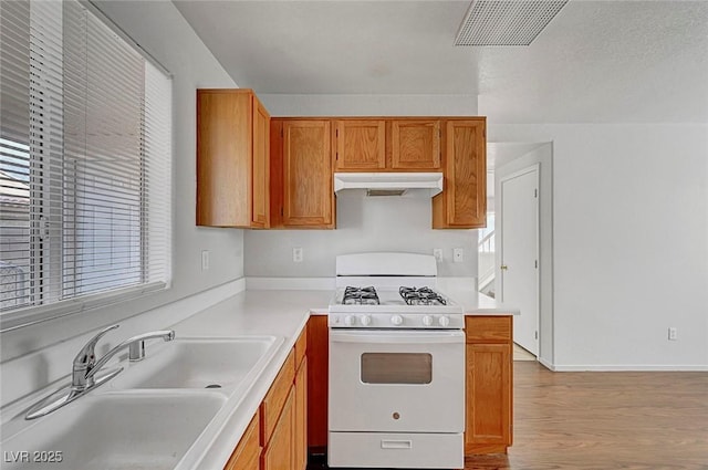 kitchen featuring visible vents, white range with gas stovetop, a sink, under cabinet range hood, and brown cabinets