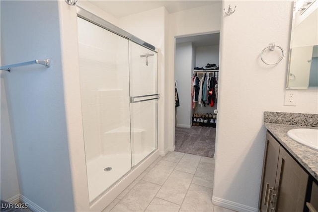 bathroom with a shower stall, a walk in closet, baseboards, tile patterned floors, and vanity