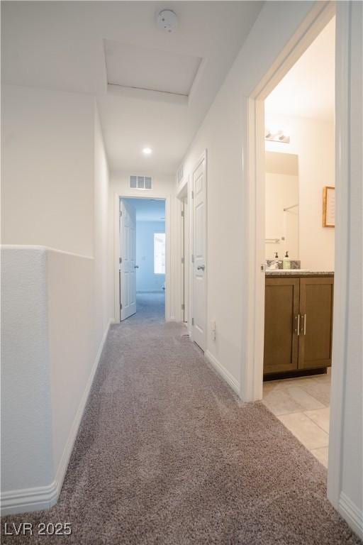 hall with baseboards, visible vents, light carpet, and attic access