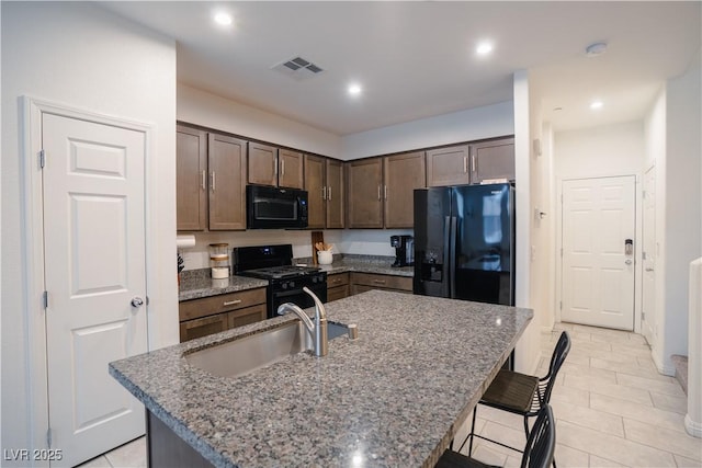 kitchen with a center island with sink, visible vents, a sink, black appliances, and a kitchen bar