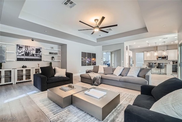 living room with visible vents, light wood-style flooring, a raised ceiling, and a ceiling fan