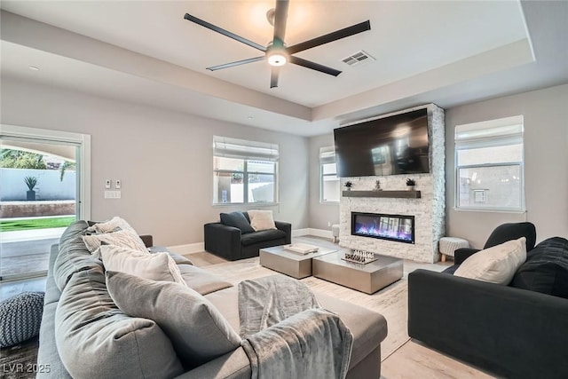 living area with a tray ceiling, plenty of natural light, visible vents, and ceiling fan