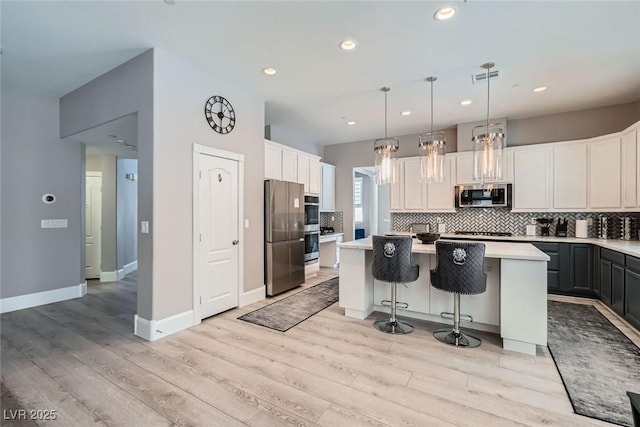 kitchen featuring light wood-style flooring, tasteful backsplash, a kitchen island, appliances with stainless steel finishes, and light countertops