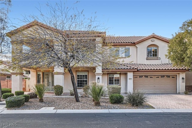 mediterranean / spanish house with stucco siding, an attached garage, driveway, and a tiled roof