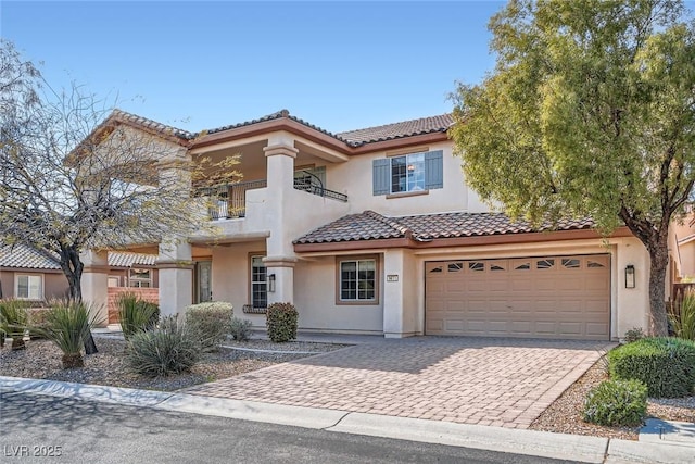 mediterranean / spanish house featuring a balcony, driveway, an attached garage, stucco siding, and a tiled roof