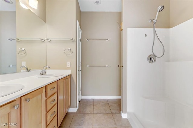 bathroom with baseboards, double vanity, a sink, tile patterned flooring, and a shower