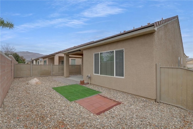 rear view of house featuring stucco siding, a patio, a fenced backyard, and a mountain view