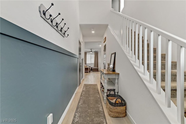 hall featuring light wood finished floors, stairs, and baseboards