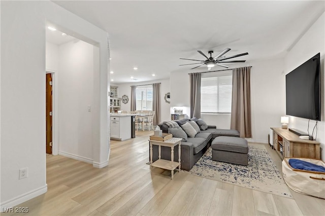 living room with ceiling fan, baseboards, and light wood-style floors