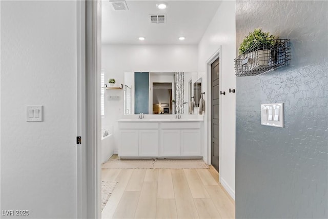 bathroom with double vanity, visible vents, a tub to relax in, and a sink