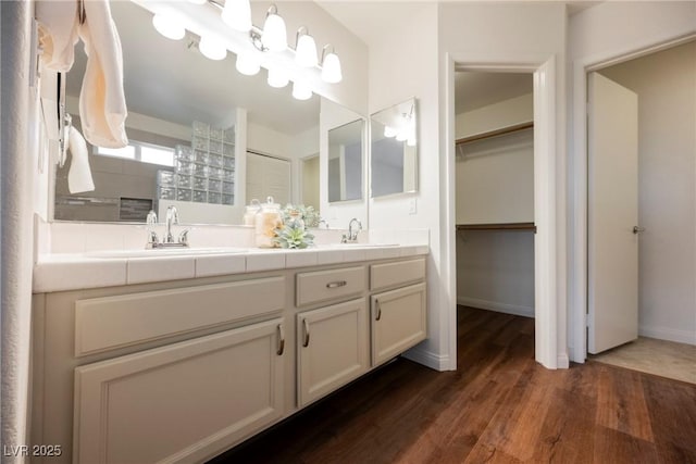 bathroom featuring double vanity, a spacious closet, wood finished floors, and a sink