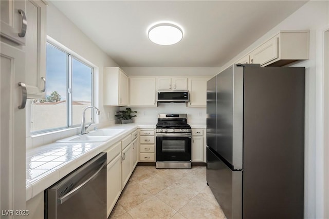 kitchen with tile countertops, light tile patterned floors, a sink, stainless steel appliances, and white cabinets