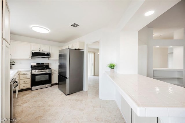 kitchen featuring light tile patterned floors, visible vents, a peninsula, stainless steel appliances, and white cabinets