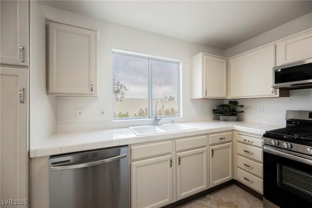 kitchen with tile countertops, light tile patterned floors, a sink, appliances with stainless steel finishes, and white cabinetry