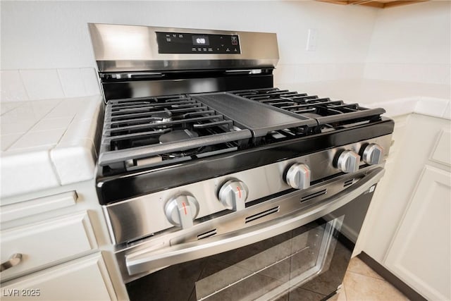 interior details with tasteful backsplash, stainless steel range with gas cooktop, white cabinets, and light countertops