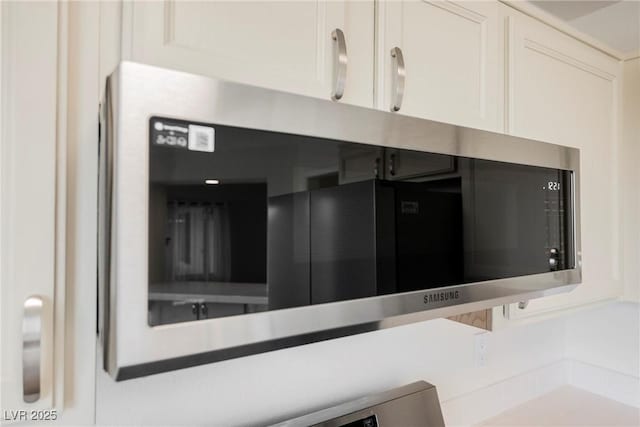 room details with stainless steel microwave, white cabinetry, and light countertops