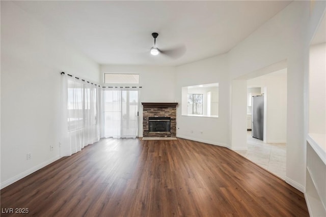 unfurnished living room with baseboards, a fireplace, wood finished floors, and a ceiling fan