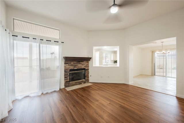 unfurnished living room with ceiling fan with notable chandelier, wood finished floors, baseboards, and a fireplace