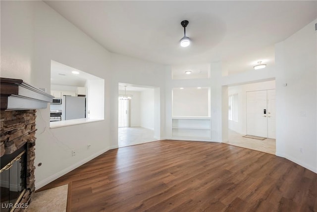 unfurnished living room featuring a chandelier, baseboards, wood finished floors, and a fireplace