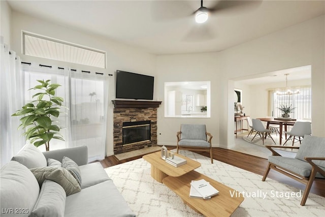 living room with baseboards, wood finished floors, a fireplace, and ceiling fan with notable chandelier