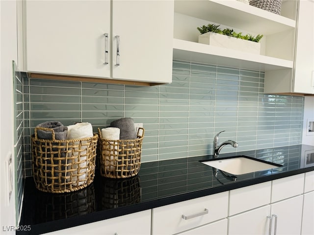 kitchen with dark countertops, a sink, backsplash, white cabinets, and open shelves