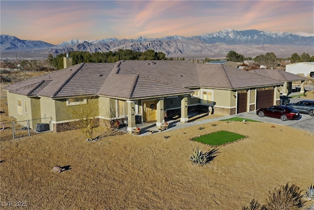 view of front of home with fence, stucco siding, a garage, stone siding, and a mountain view