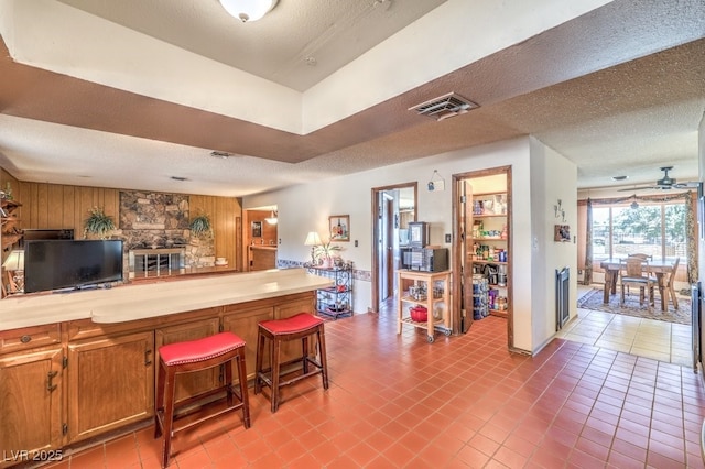 10615 Rancho Destino Rd, Las Vegas, NV 89183 - kitchen with visible vents, brown cabinets, a textured ceiling, a breakfast bar area, and wood walls