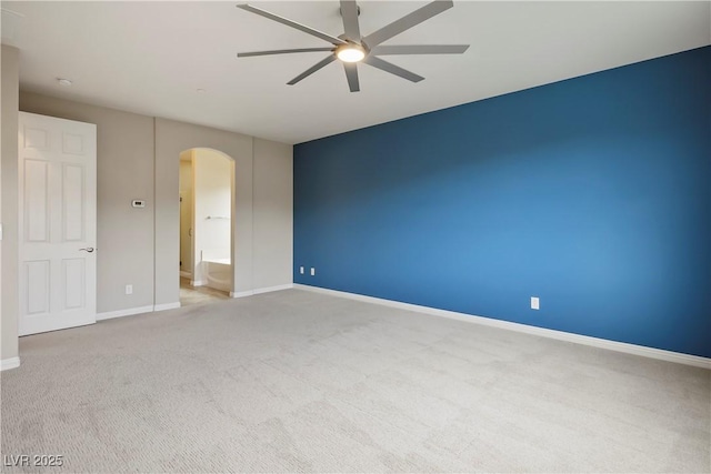 carpeted empty room featuring a ceiling fan, arched walkways, and baseboards