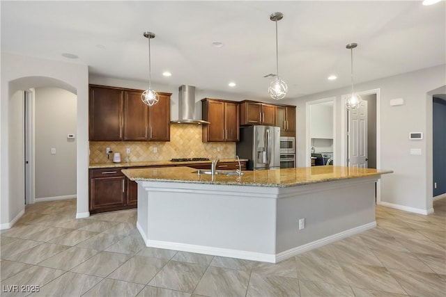 kitchen with arched walkways, a sink, stainless steel appliances, washer and dryer, and wall chimney range hood