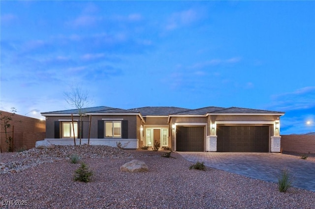 prairie-style home featuring stucco siding, decorative driveway, a garage, and fence