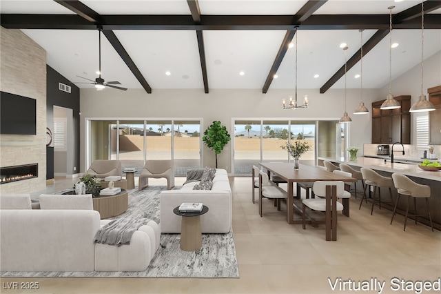 living room with visible vents, high vaulted ceiling, beam ceiling, ceiling fan with notable chandelier, and a large fireplace