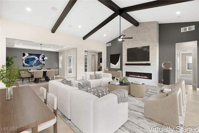 living area featuring visible vents, beamed ceiling, high vaulted ceiling, a ceiling fan, and a fireplace