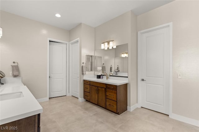 full bath featuring a sink, baseboards, and two vanities