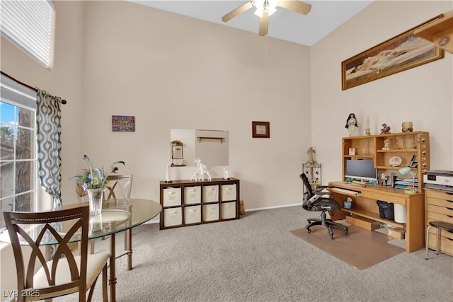 office area featuring carpet floors, a healthy amount of sunlight, a towering ceiling, and a ceiling fan