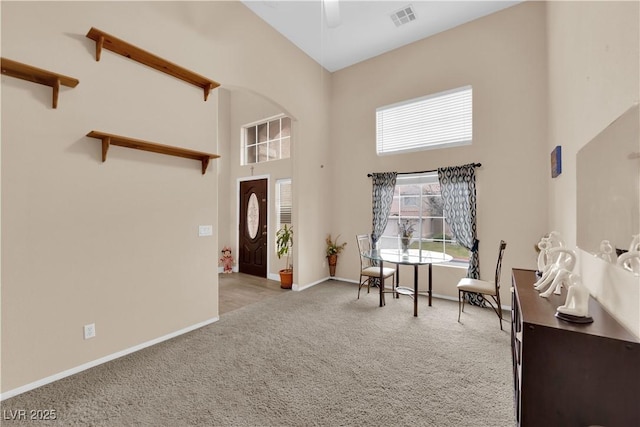 foyer with visible vents, baseboards, carpet flooring, a high ceiling, and arched walkways