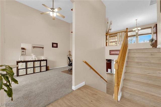 stairs with carpet, wood finished floors, baseboards, a high ceiling, and ceiling fan with notable chandelier