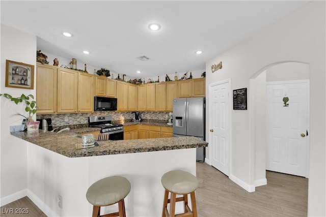 kitchen featuring a peninsula, light wood-style flooring, light brown cabinetry, appliances with stainless steel finishes, and a kitchen bar