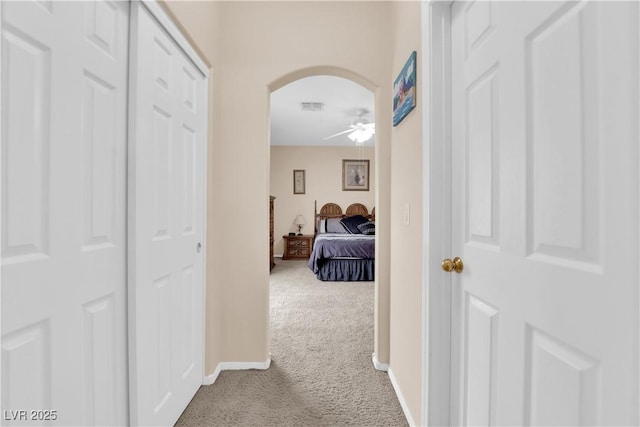 corridor featuring baseboards, carpet, visible vents, and arched walkways