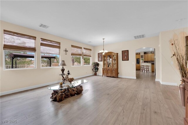 living room with baseboards, visible vents, arched walkways, a notable chandelier, and light wood-type flooring