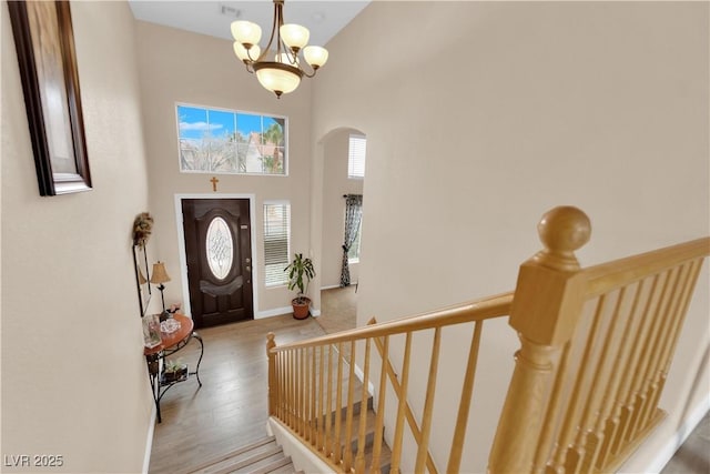 foyer entrance with baseboards, a towering ceiling, wood finished floors, arched walkways, and a notable chandelier