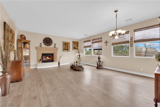 unfurnished living room featuring light wood-type flooring, visible vents, a glass covered fireplace, baseboards, and a chandelier