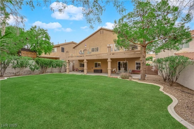 back of house featuring a balcony, a fenced backyard, stucco siding, a patio area, and a lawn