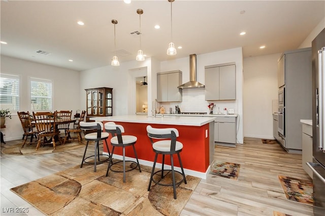 kitchen featuring oven, gray cabinetry, light wood-style floors, wall chimney range hood, and tasteful backsplash