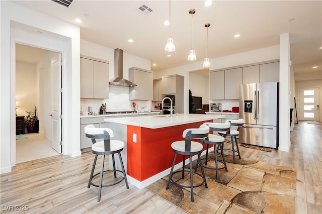 kitchen featuring visible vents, gray cabinetry, a breakfast bar, stainless steel appliances, and wall chimney exhaust hood