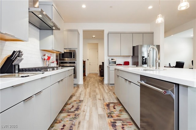 kitchen with modern cabinets, gray cabinetry, a sink, stainless steel appliances, and wall chimney exhaust hood