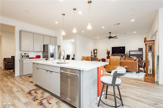 kitchen featuring visible vents, gray cabinetry, a kitchen island with sink, a ceiling fan, and light countertops