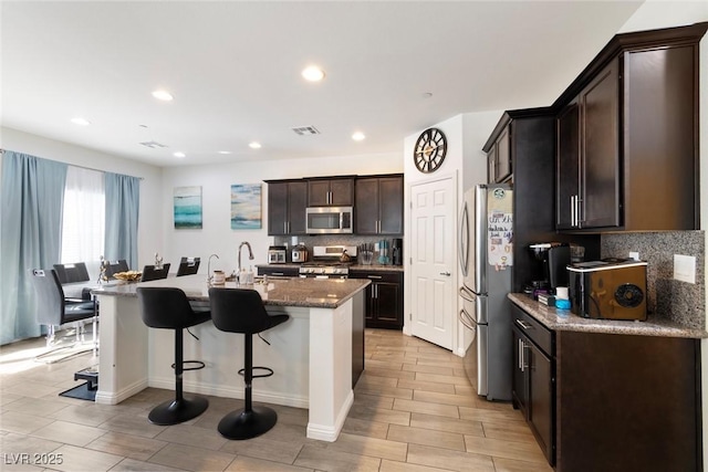 kitchen featuring a kitchen bar, visible vents, stainless steel appliances, decorative backsplash, and dark brown cabinets