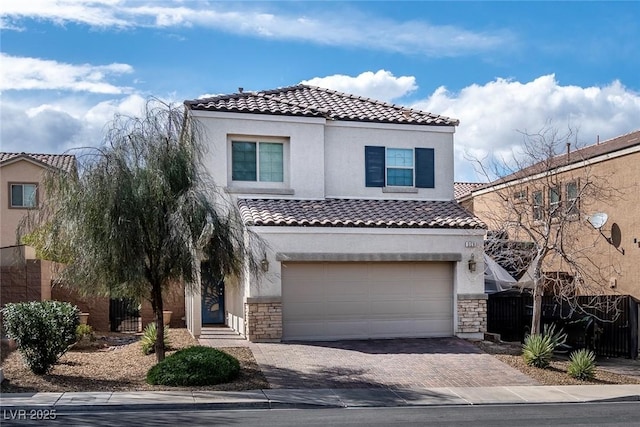 mediterranean / spanish-style home with stone siding, a tiled roof, an attached garage, and decorative driveway