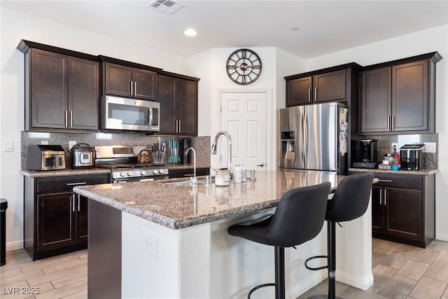 kitchen featuring visible vents, wood tiled floor, a breakfast bar, appliances with stainless steel finishes, and tasteful backsplash